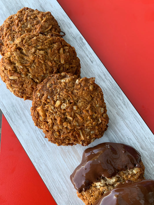 Three ANZAC cookies made from a very easy recipe sit on a white tray on a red table